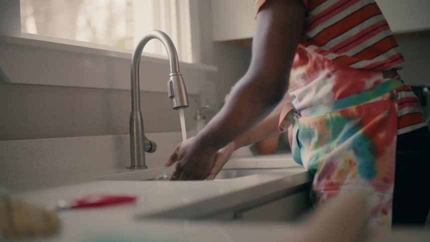 A person wearing an apron washes their hands in a kitchen faucet