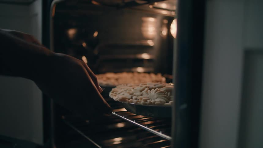 A man at home puts a pie in the oven and closes the door
