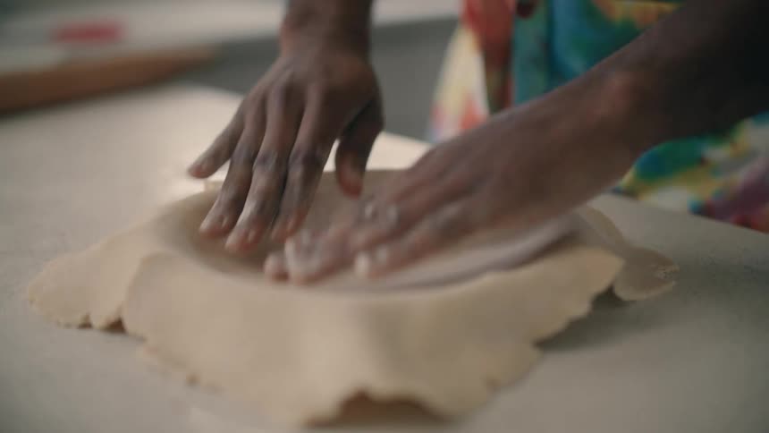 Woman places a sheet of pie dough over a steel pie baking pan in the kitchen at home