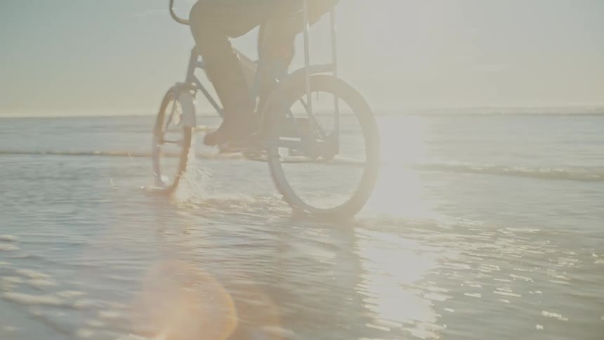 A child is riding a bike on the beach coast at dusk