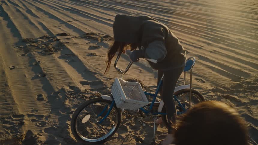 A girl gets on the bike on the beach