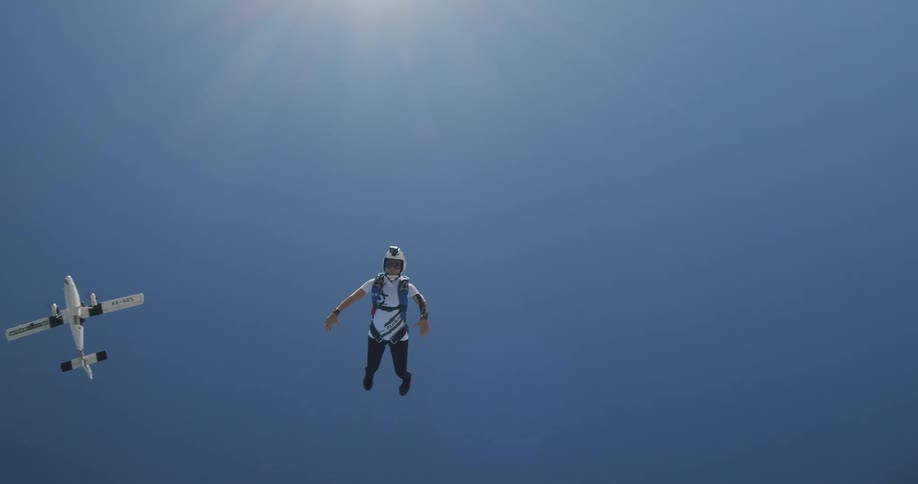 A skydiver wearing a helmet and a parachute drops from an airplane and slowly falls to the ground