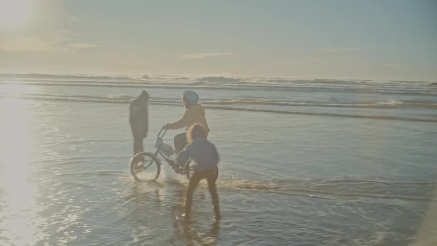 A girl rides a bike through waves on the beach