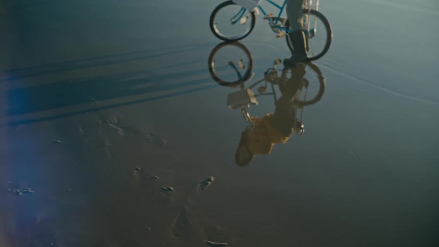 A female is trying to ride a bicycle on beach and her reflection is visible in sand