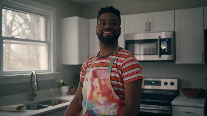 A man is smiling in his kitchen next to a window