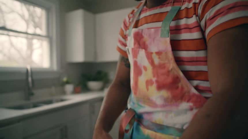 A man is standing in a kitchen and cutting the edges from pie crust with scissors