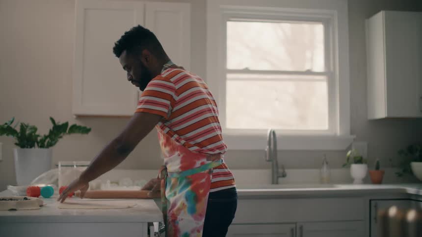 A man uses a rolling pin to flatten dough in a home kitchen during the day