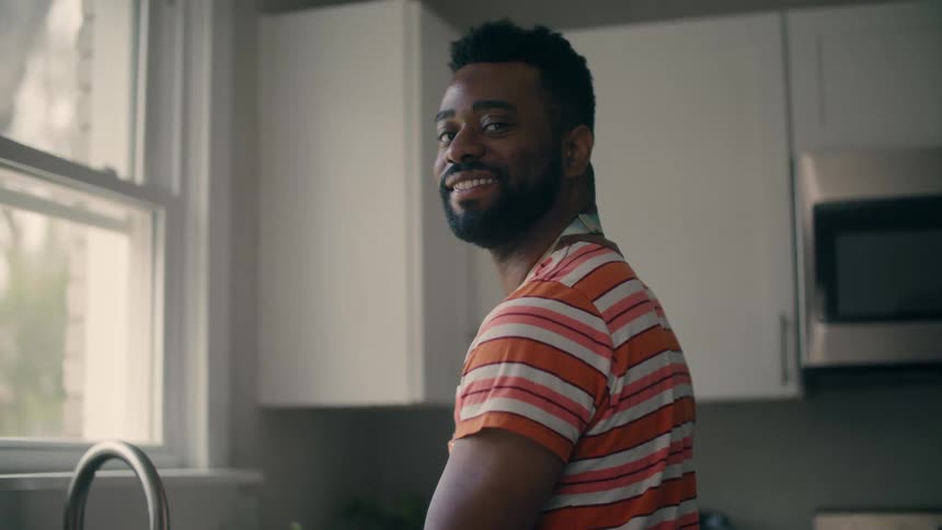 Man with beard and striped tshirt does the dishes in the kitchen smiling