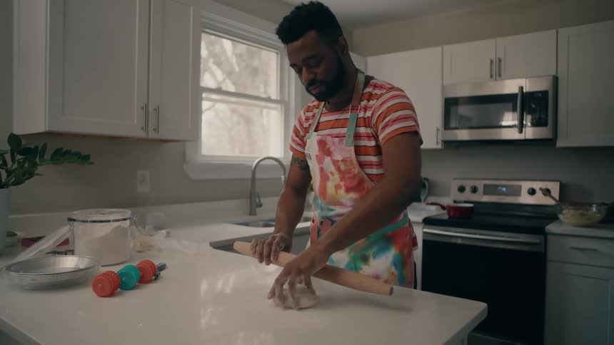 Man wearing colorful apron rolls dough on counter top