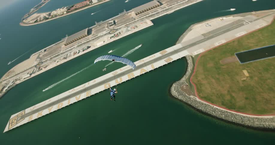 A person skydives over the water and heads towards the shore