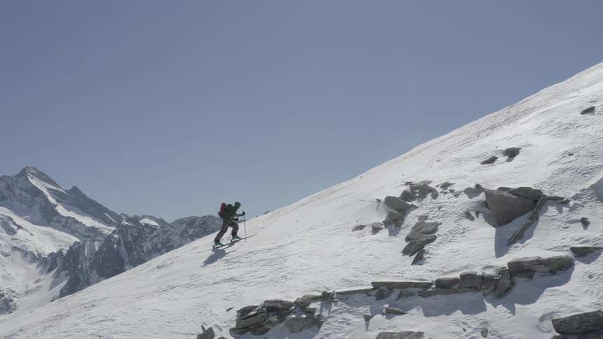 A person with skis on walks up a snowy mountain
