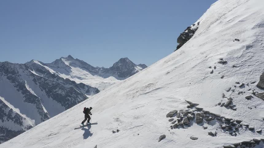 A person with skis on climbs up a snowy mountain