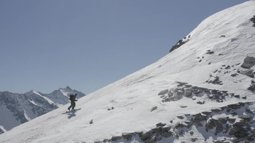 A mountaineer climbs a snowy mountain slope using trekking poles during the day