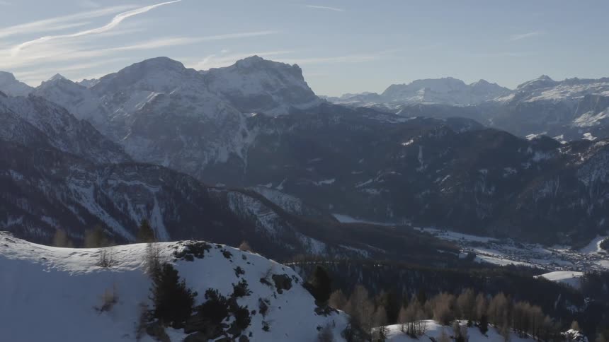 Snow covered forested mountains and a valley below under a cloudy sky