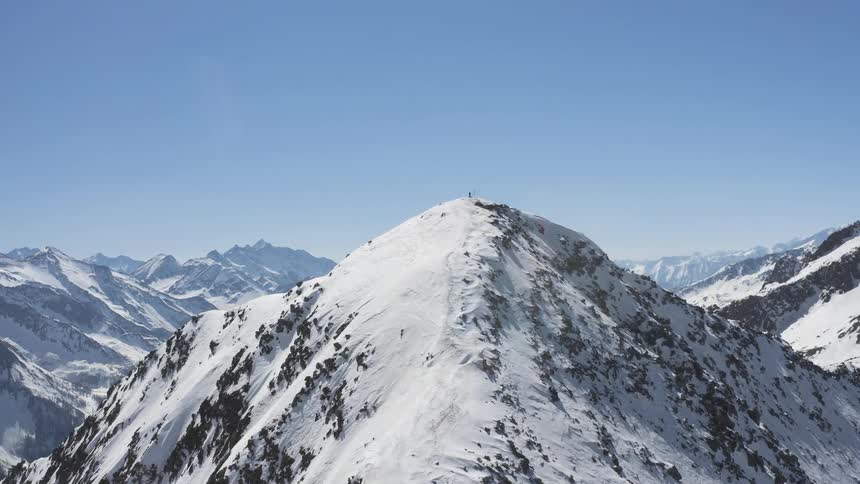 Aerial view of a man standing on the summit of a snow covered peak on a mountain range