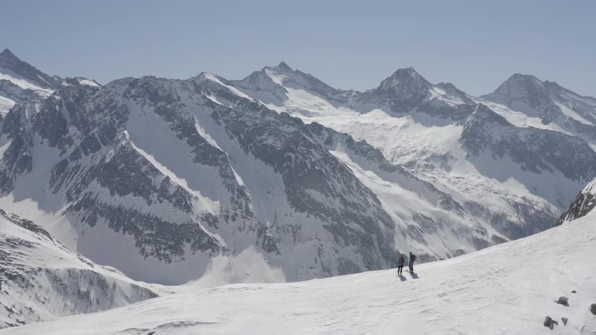 A pair of mountaineers standing high in snowy mountains look out over the valley below