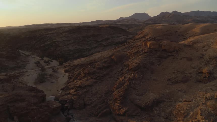 Aerial over desert river and mountains at dusk