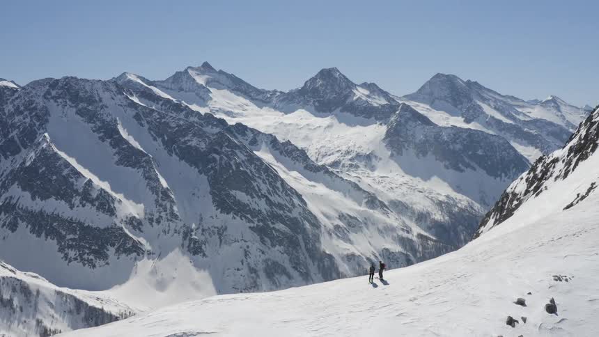 A pair of mountaineers standing atop a mountain look out at the landscape below