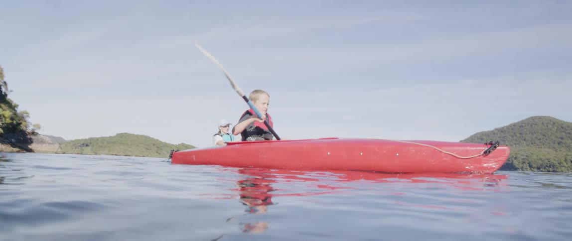 A boy paddles a kayak across the ocean while an adult woman paddles another kayak beside him