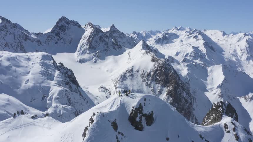 Aerial view of a group of skiers standing on the peak of a snow covered mountain