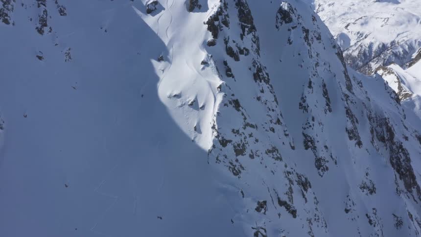 A skier skis down a steep slope high in the mountains on a clear day