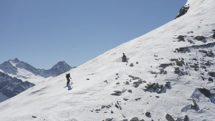 A man wearing skis is hiking up the ridge of a snow covered mountain