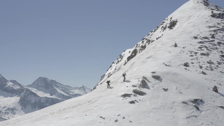 A pair of mountaineers hike up a snowy mountain ridge during the day