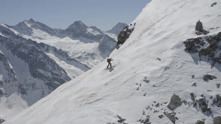 A mountaineer climbs a snowy mountain slope on a clear day