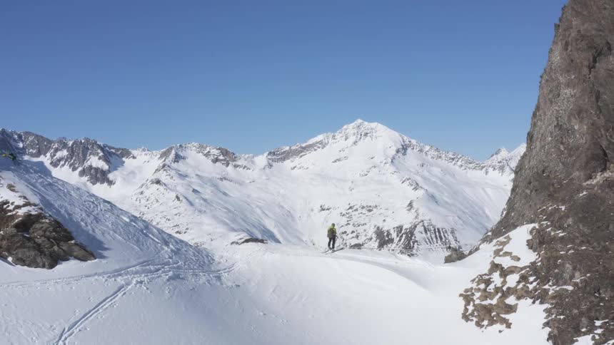 A skier standing on a cliff high in the mountains looks out over the landscape below