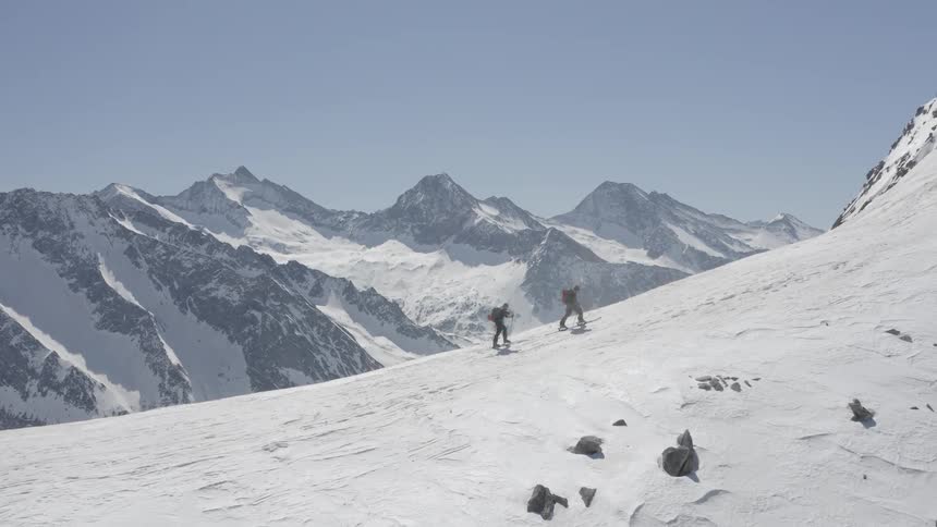 A pair of mountaineers climb a snowy mountain slope on a clear day