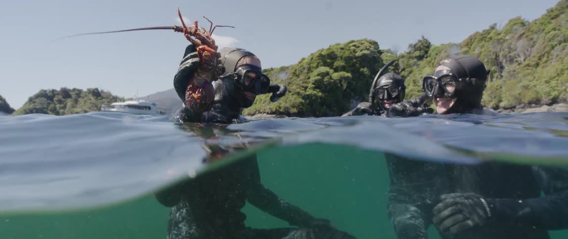 Diver showing his partners a lobster while floating on the surface of a beach