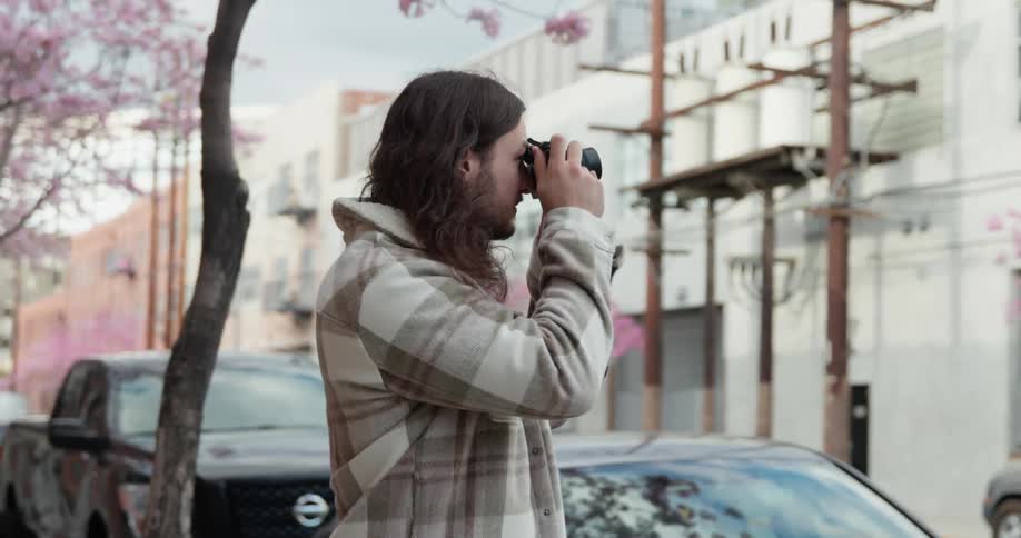 Young long haired man takes pictures of the flowering cherry trees on the streets