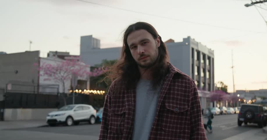 Man stands on sidewalk and smiles as person leads dog across street in background