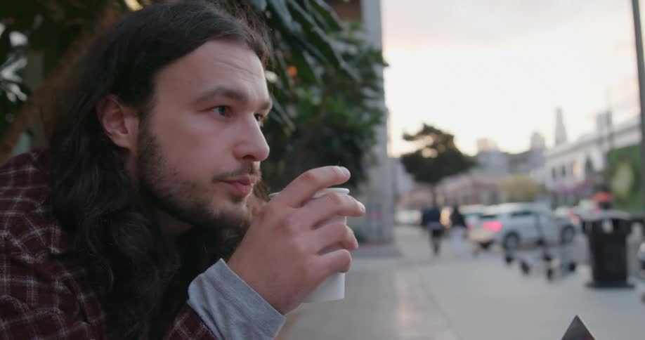 A man sits and slowly takes a sip from his coffee cup while looking out at the surrounding neighborhood