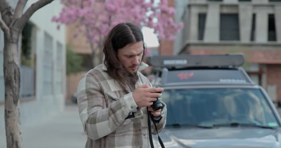 Male photographer stands near flowering tree and a car while taking a picture