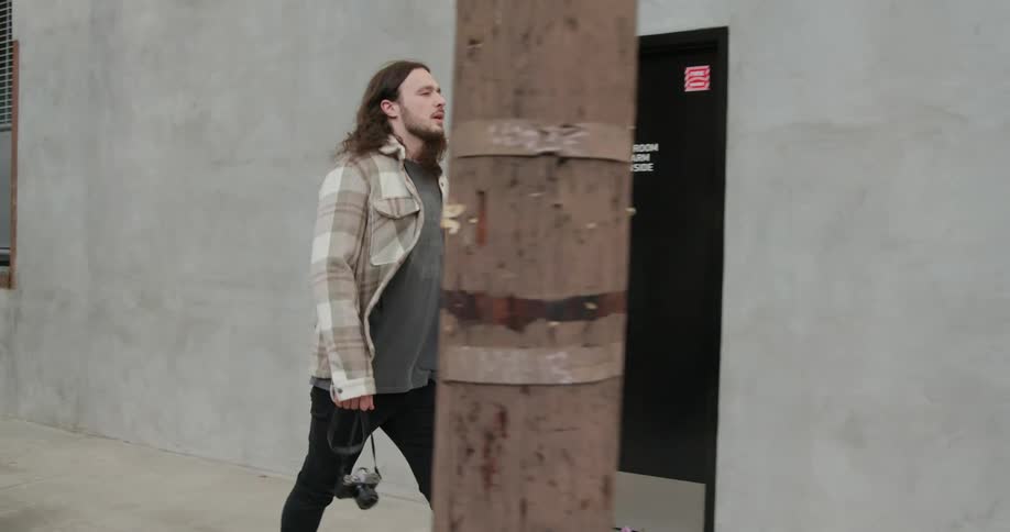 Photographer walks along sidewalk carrying camera by the strap