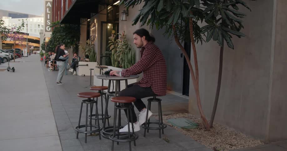 Photographer smiles while typing on laptop at outdoor cafe