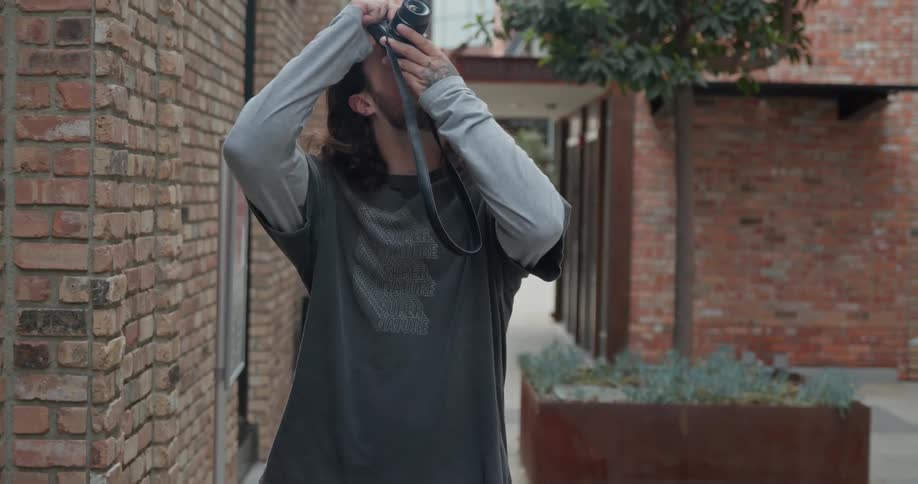 Young long haired walking on the city takes pictures of the buildings