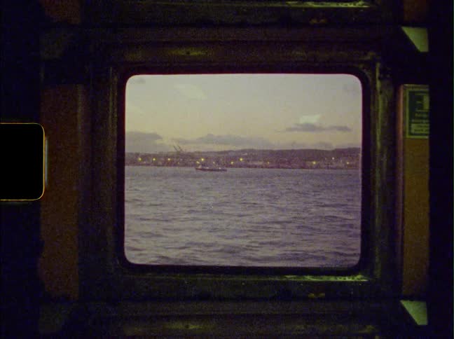 A small window in boat shows views of a neighborhood across the sea