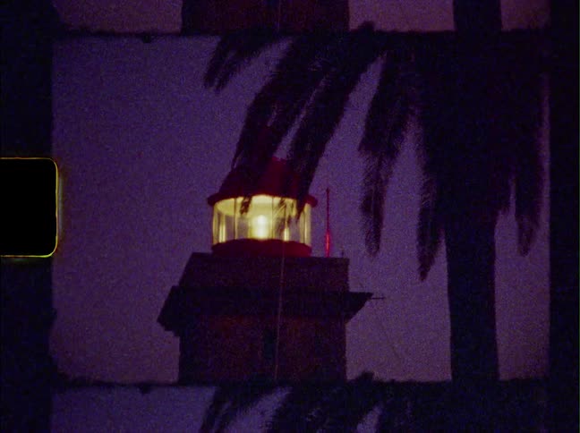 A light is flashing inside a lighthouse at night