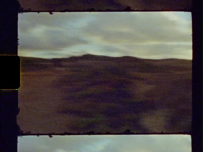 Person with a backpack walking near the ocean at sunset caught on vintage film