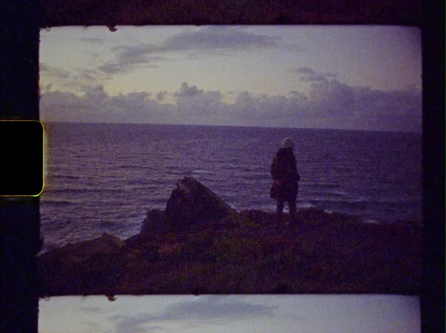 A woman stands on the edge of rocks overlooking the ocean