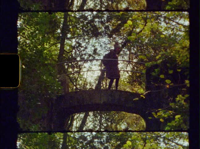 A woman wearing a backpack walks over a small bridge located in an area surrounded by trees