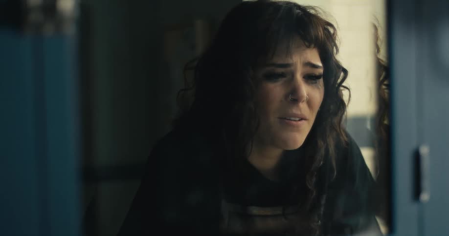 A woman cries and covers her face as she can be seen in the reflection of a mirror
