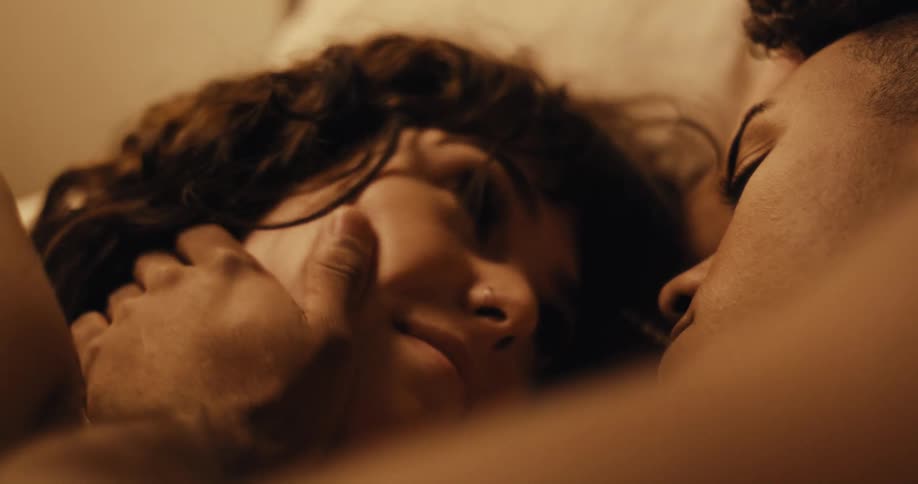 A man caresses his girlfriends face while they cuddle in bed