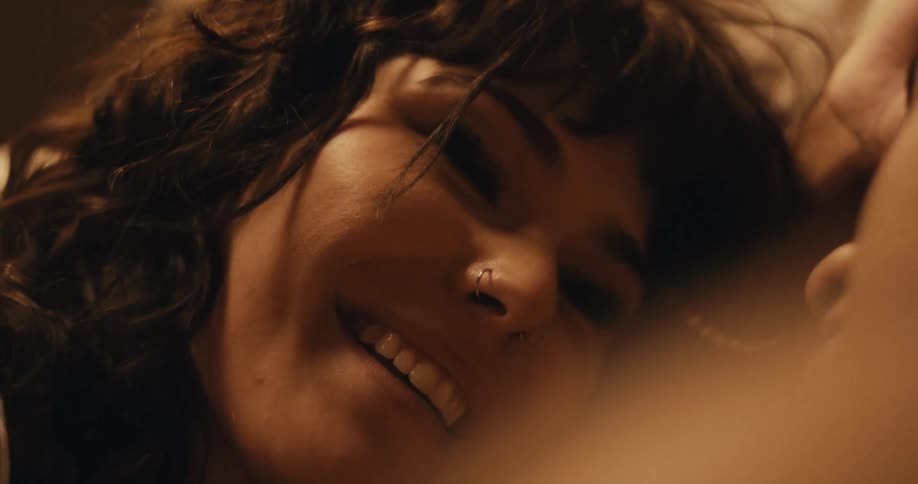 A woman wearing a nose ring is laying down with another person and smiling at them