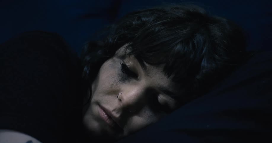 A woman wearing a nose ring is sleeping in the dark
