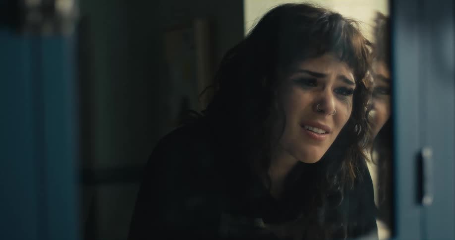 A woman cries while looking at herself in the mirror in a public restroom
