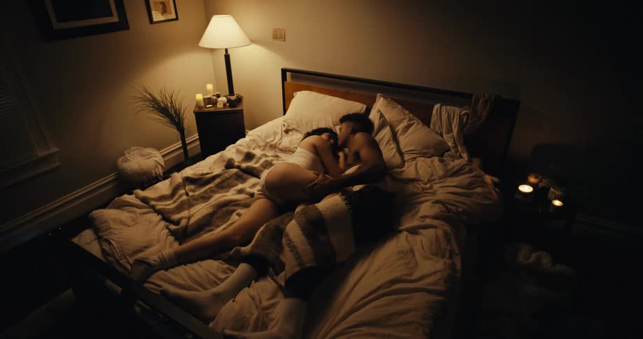 A woman turns to cuddle with her boyfriend in bed and places her leg over his