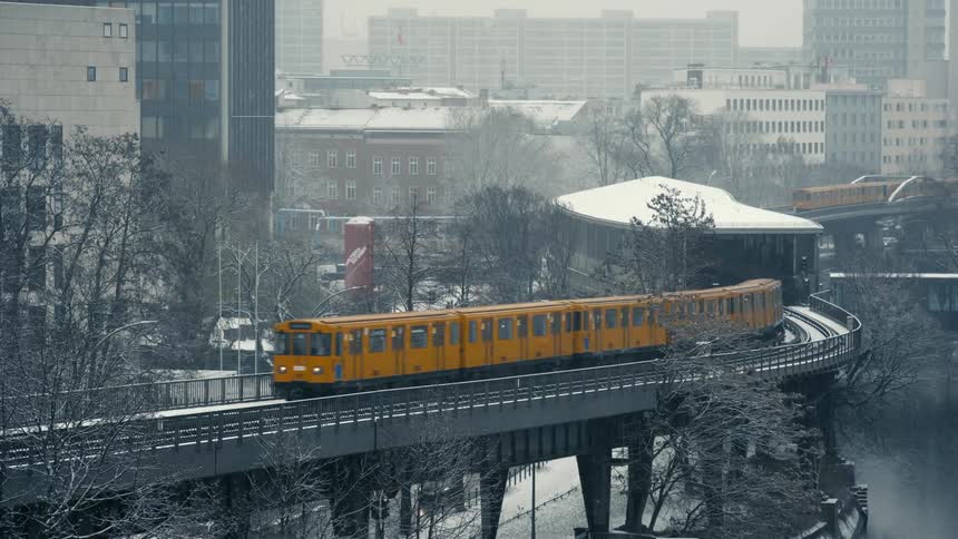 Yellow train leaving a station over the street of a city under a snow storm